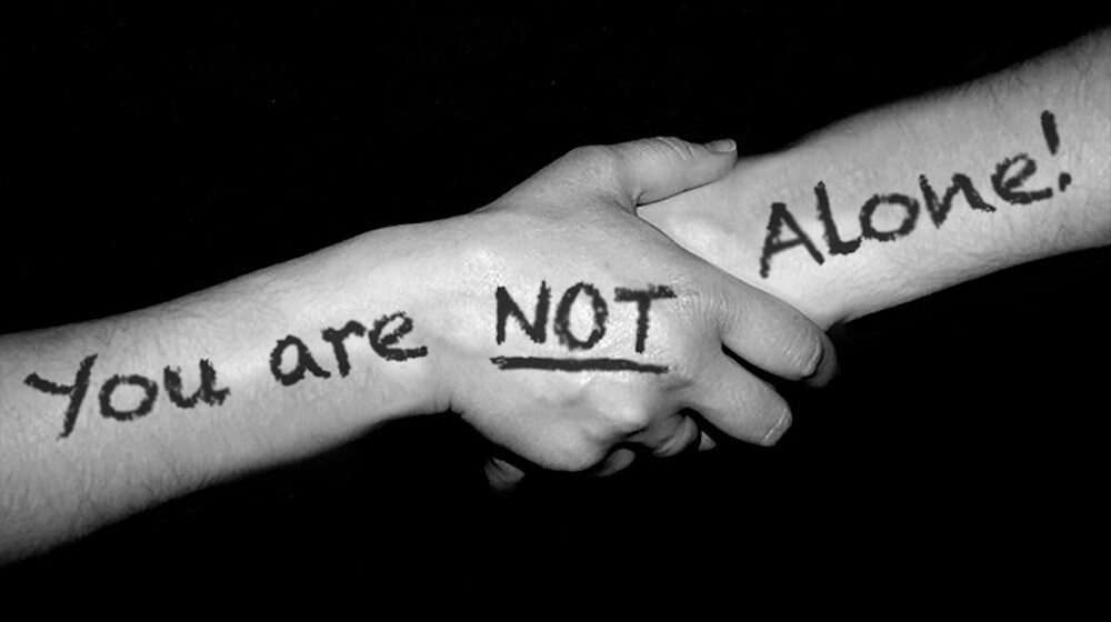 Hands holding with message you are not alone, proving storytelling heals through connection